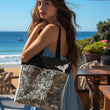 Women wearing a blue summer dress and holding the 'Ocean White' tote bag by Studio Bilby. Background of beachside cafe and blue sky.