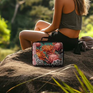 Waratah insulated lunchbox by Studio Bilby sitting on a rock next to women. Background of eucalyptus forest.